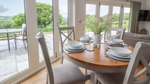 A dining area with a table set for six, large windows, and a view of greenery outside. - Pen Bryn (Ruthin)