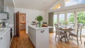 A modern kitchen with a central island, wooden flooring, and a dining area with a view. - Pen Bryn (Ruthin)