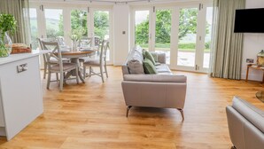 A spacious living area with a dining table, sofa, and large windows offering a view of the outdoors. - Pen Bryn (Ruthin)