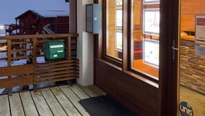 En træterrasse med en glasdør, der fører til et rum med udsigt til en bygning.