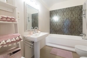 A bathroom with a white sink, mirror, and bathtub. There are pink towels and a pink rug on the floor. - Summer Seaside Pearl Apartment Kastela (Kastela)