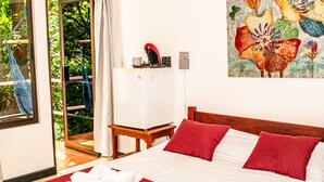 A hotel room with a bed, red and white bedding, a painting on the wall, and a view of greenery through the window. - VAL HOTEL MANUEL ANTONIO (Quepos)