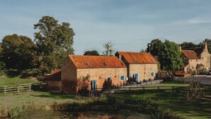 Un edificio de piedra tradicional con tejado rojo, rodeado de un césped y una pequeña masa de agua.