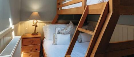 Un letto a castello in una stanza con soffitto spiovente, un comodino con cassetti e una lampada.