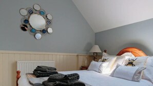 Una cama bien hecha con una manta gris y toallas dobladas, cabecera de madera y un espejo con marco circular fijado a la pared.