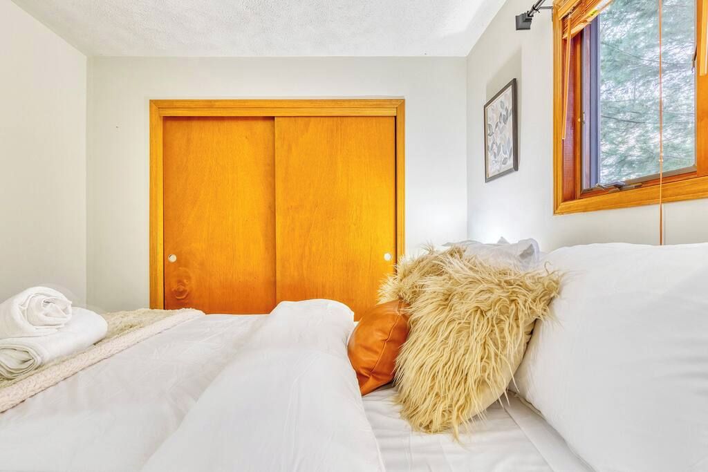 Een slaapkamer met een houten deur, een bed met witte lakens en een raam met uitzicht op bomen.