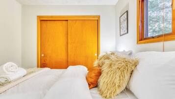 Een slaapkamer met een houten deur, een bed met witte lakens en een raam met uitzicht op bomen.