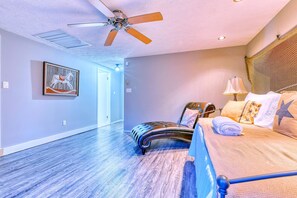 Quarto com cama, cadeira, ventilador de teto e uma pintura na parede.
