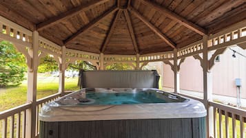A hot tub under a wooden gazebo with a view of a grassy yard.