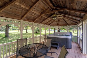 A covered outdoor patio with a hot tub, wooden deck, and a table with chairs. - Antler Ridge: 3BDR w/ Hot Tub & Game Room (Penn Forest Township)