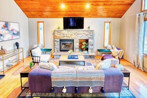 A cozy living room with a stone fireplace, comfortable seating, and a flat-screen TV mounted above it.