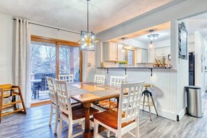 A dining area with a wooden table and chairs, a kitchen with white cabinets, and a view through a glass door. - Antler Ridge: Hot Tub Golf Simulator Game Room (Penn Forest Township)
