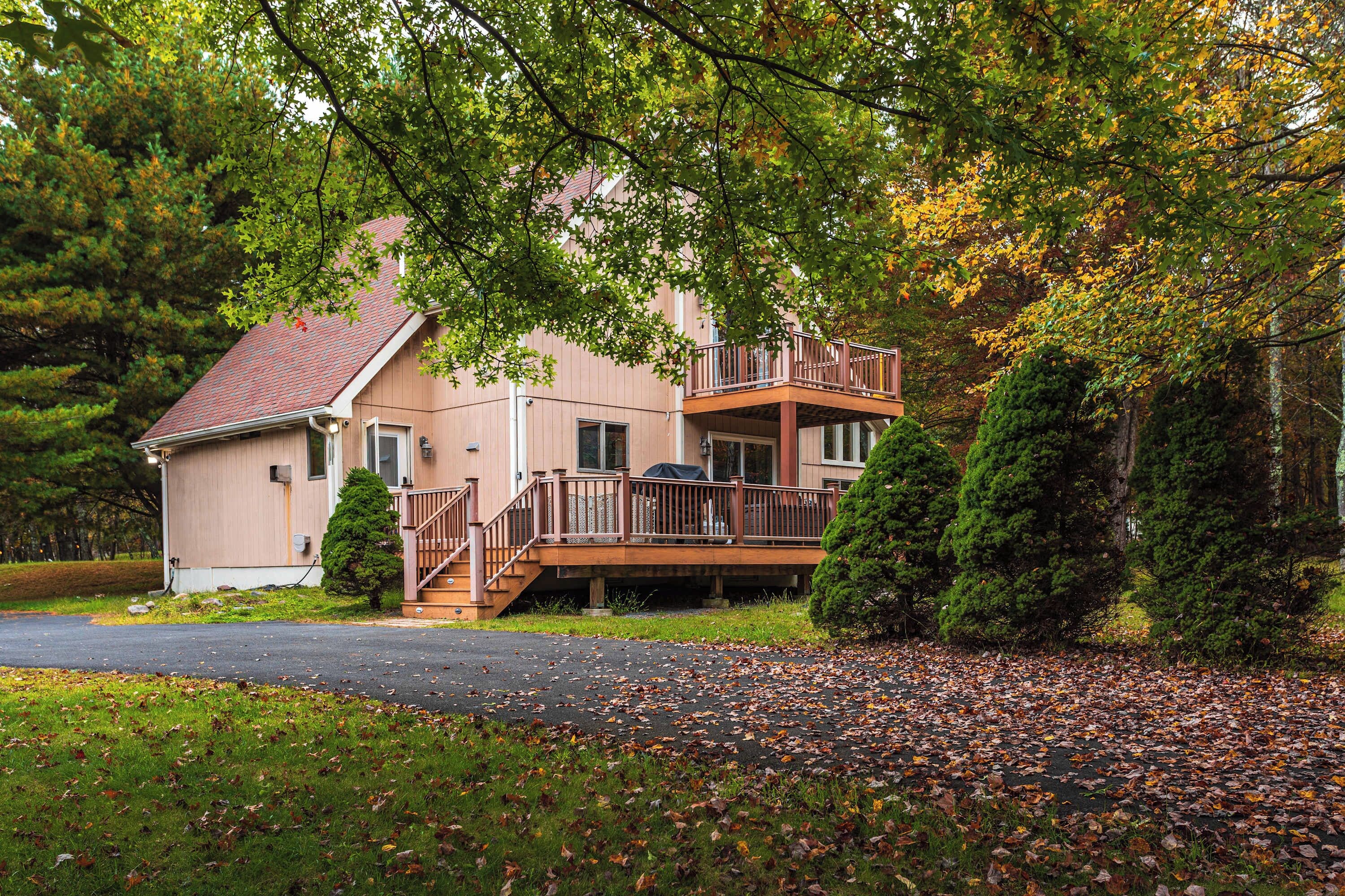 A two-story house with a balcony, surrounded by trees and a driveway.