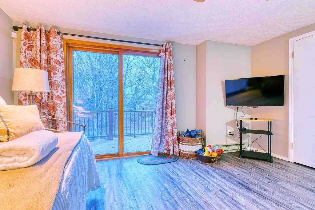 Une chambre avec un lit, une télévision, une fenêtre avec des rideaux et une vue sur les arbres à l’extérieur.