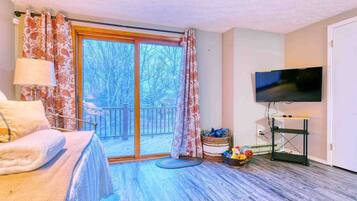 Une chambre avec un lit, une télévision, une fenêtre avec des rideaux et une vue sur les arbres à l’extérieur.