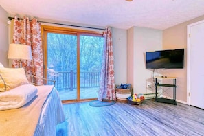 A room with a bed, a television, a window with curtains, and a view of trees outside. - Antler Ridge: 3BDR w/ Hot Tub & Game Room (Penn Forest Township)