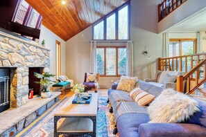 Un salon chaleureux avec une cheminée en pierre, un canapé bleu et un escalier en bois.