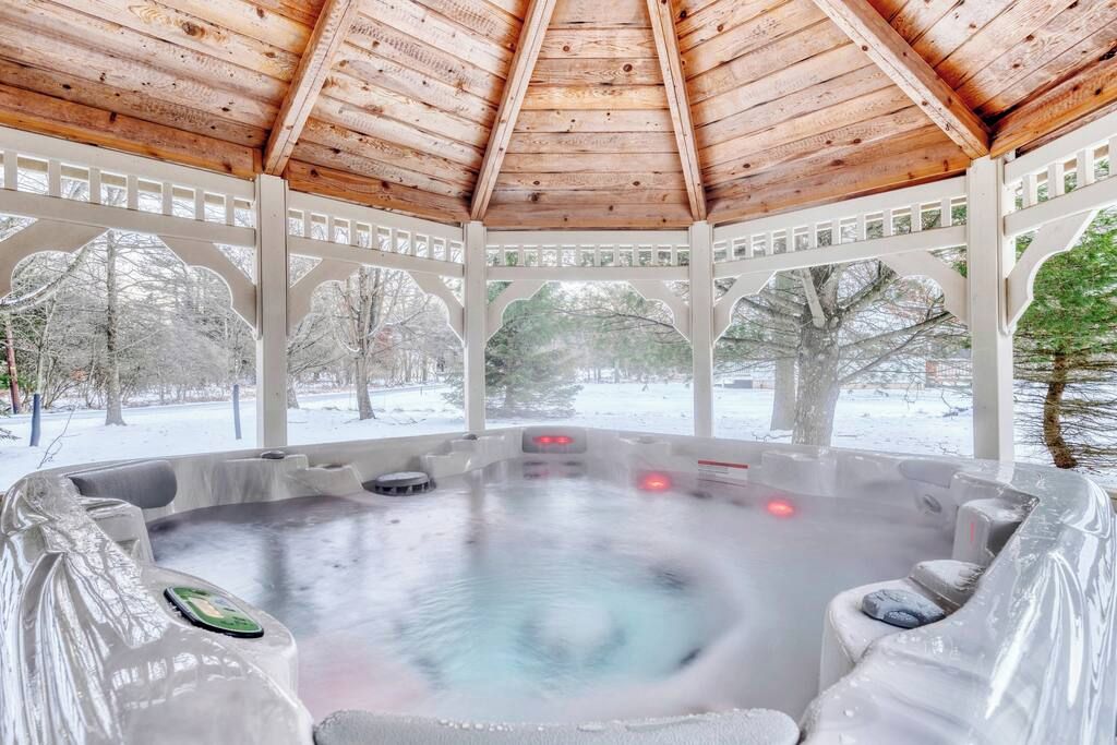 A hot tub under a wooden gazebo with a view of a snowy landscape.