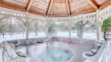 A hot tub under a wooden gazebo with a view of a snowy landscape.