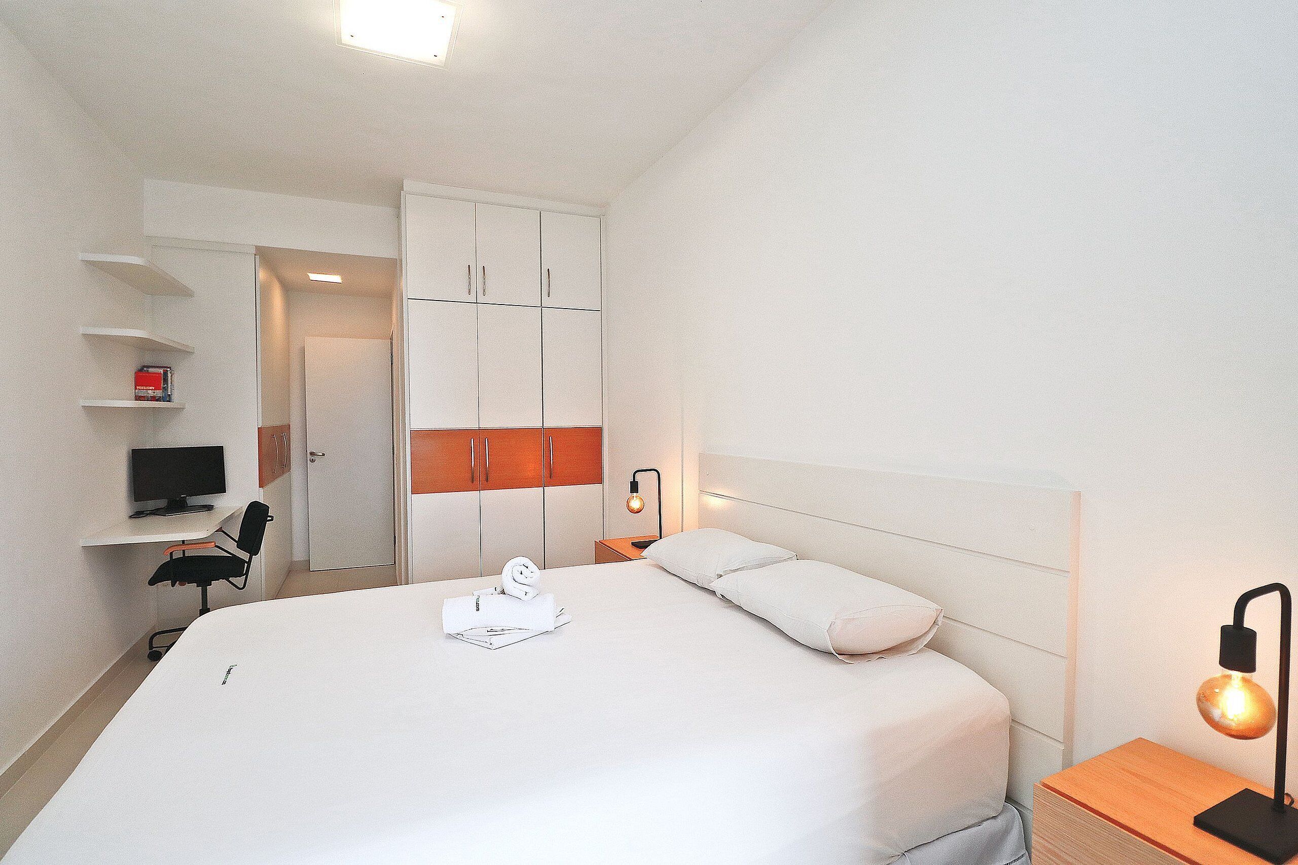 Une chambre d’hôtel bien rangée, avec un lit, une table de chevet, une lampe et un bureau avec une chaise.