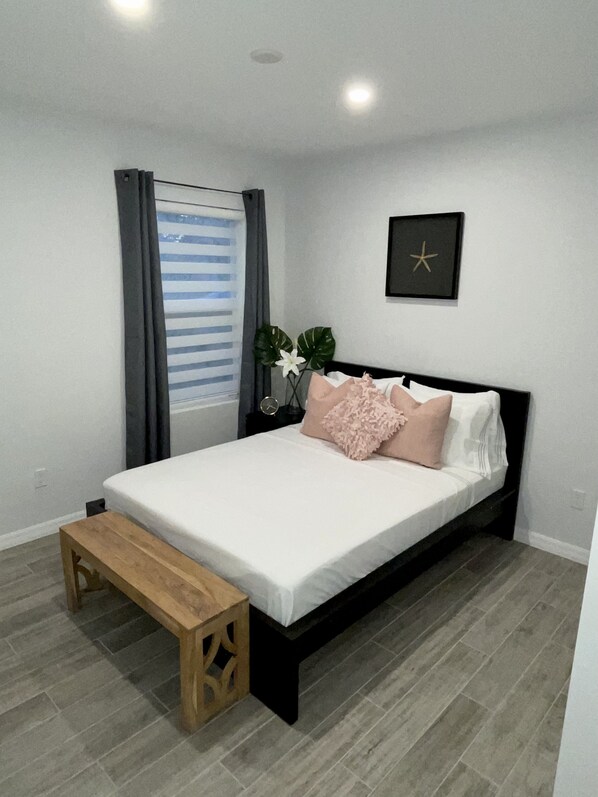 A bedroom with a bed, a bench, a window with curtains, a plant, and a wall-mounted star decoration.