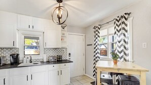 A modern kitchen with white cabinets, a black countertop, and a wooden table. - Colorado Cottage! Downtown Home on OCC w/ Patio! (Colorado Springs)
