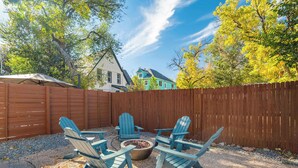 A backyard with a wooden fence, a fire pit, and Adirondack chairs. - Colorado Cottage! Downtown Home on OCC w/ Patio! (Colorado Springs)