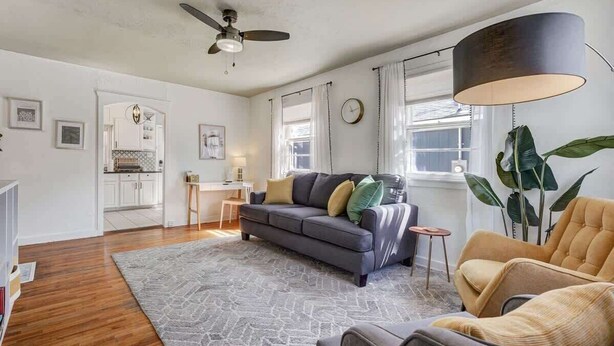 A spacious living room with a grey sofa, a yellow armchair, and a coffee table. There is a kitchen in the background with white cabinets and a dining area. - Colorado Cottage! Downtown Home on OCC w/ Patio! (Colorado Springs)