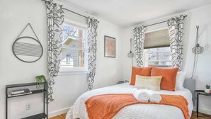 A bedroom with a bed, a bedside table, a wall-mounted light, and a window with curtains. - Colorado Cottage! Downtown Home on OCC w/ Patio! (Colorado Springs)