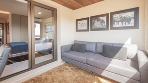 Een moderne woonkamer met een grijze bank, een grote spiegel en drie ingelijste foto’s aan de muur.