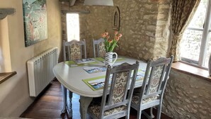 A dining area with a round table, chairs, a vase with flowers, a painting on the wall, and a window with curtains.