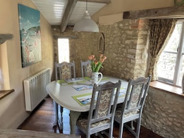 A dining area with a round table, chairs, a vase with flowers, a painting on the wall, and a window with curtains.