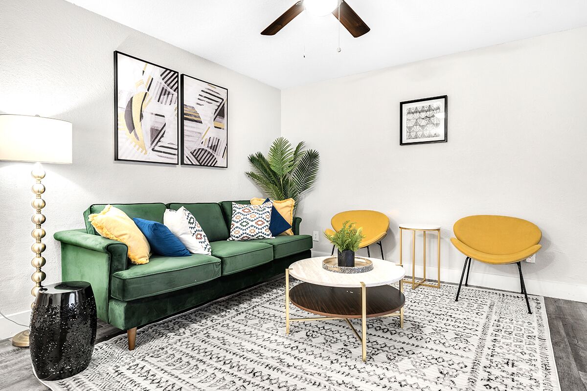 En moderne stue med en grøn sofa, gule lænestole, et rundt sofabord og abstrakt vægkunst.