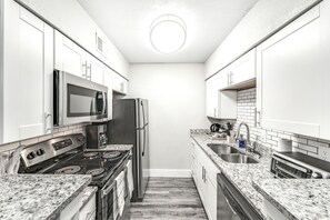 Cocina compacta con gabinetes blancos, microondas integrado, refrigerador de acero inoxidable, estufa a gas, un lavamanos y un tostador.