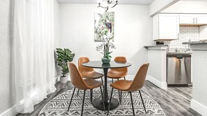 A dining area with a round table, four chairs, a vase with flowers, and a painting on the wall.