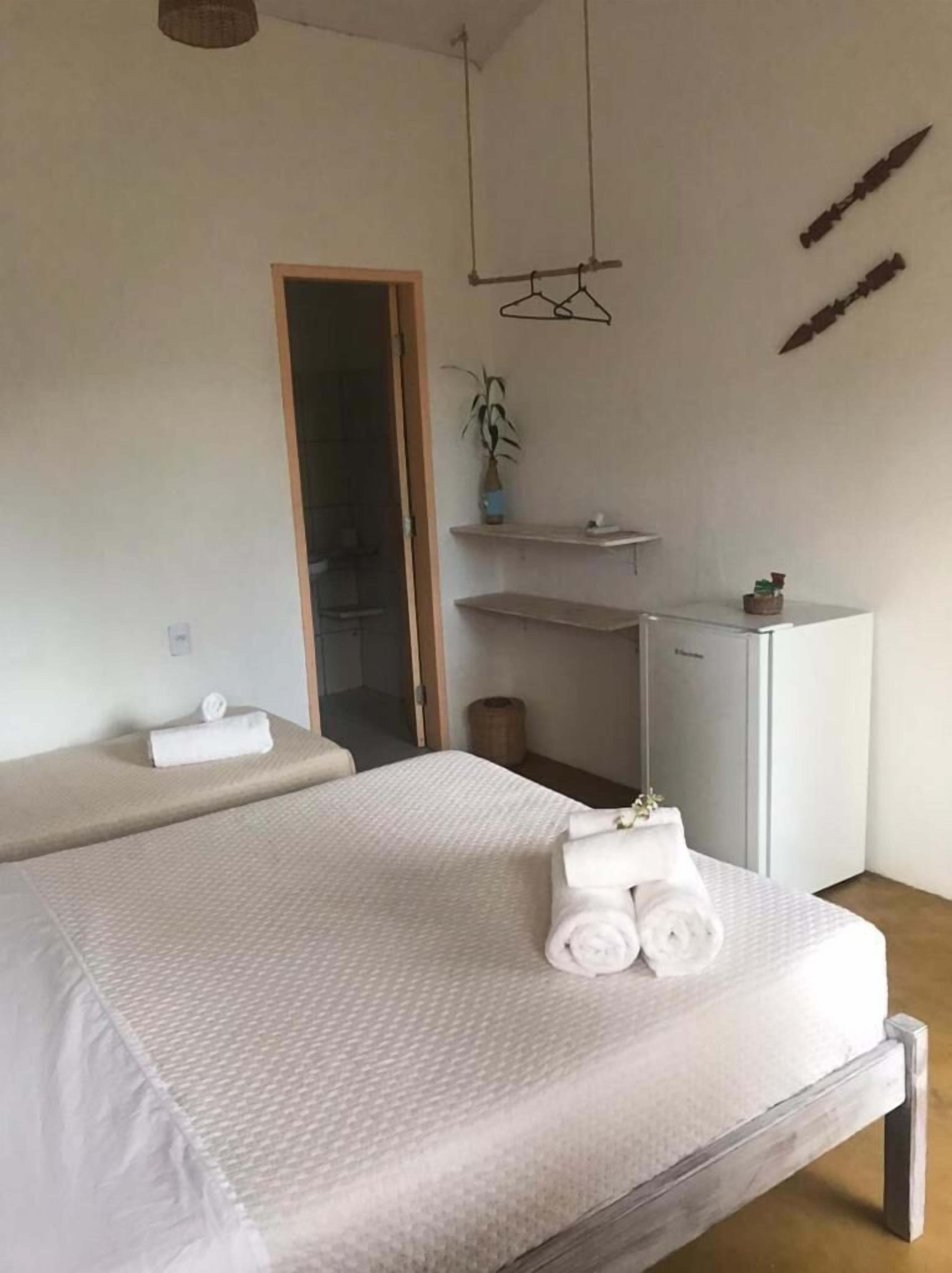 Une chambre d’hôtel minimaliste, comprenant un lit, un petit bureau, un miroir et une plante suspendue.