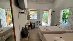 A hotel room with two beds, a TV, a mirror, and a window with a view of greenery. - Pousada Sol Nascente Caraíva (Porto Seguro)