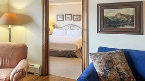 Une chambre d’hôtel avec un lit, un canapé bleu, un fauteuil en cuir marron et un tableau encadré au mur.