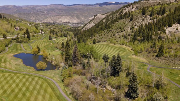 Un parcours de golf avec un étang, entouré de collines et de montagnes boisées.