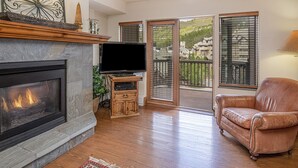 Un salon avec une cheminée, un canapé en cuir et un téléviseur posé sur un meuble en bois.