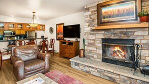 A living room with a stone fireplace, leather chair, dining table, and kitchen area with wooden cabinets. - Mountain Modern Beaver Creek Village Condo, Ski-In and Out, w/ Hot Tub and Views (Beaver Creek)