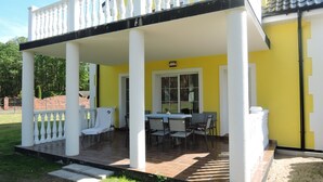 Une terrasse extérieure couverte, avec une table et des chaises, des colonnes blanches et un mur jaune.