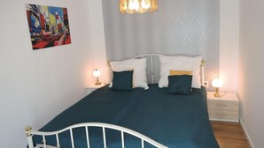 Un lit bien fait, avec une structure en métal blanc, deux tables de chevet avec des lampes et un mur à motifs derrière le lit.