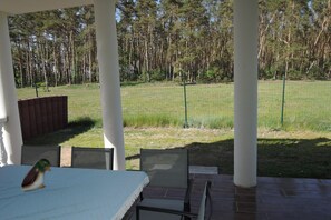 Un patio cubierto con mesa y sillas, con vistas a un campo verde y una zona boscosa.