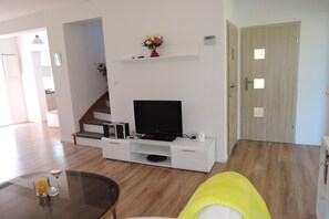 Una sala de estar moderna con un televisor de pantalla plana, un mueble blanco para equipo multimedia y una escalera que sube a otro nivel.