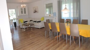 Un salon moderne comprenant un coin repas, des murs blancs, une cheminée et un lustre.