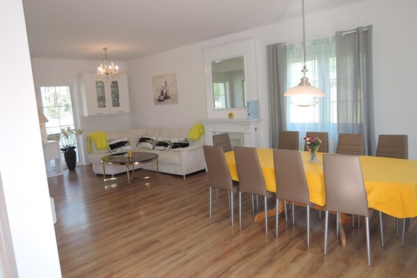 Una sala de estar moderna con comedor, paredes blancas, chimenea y candelabro.