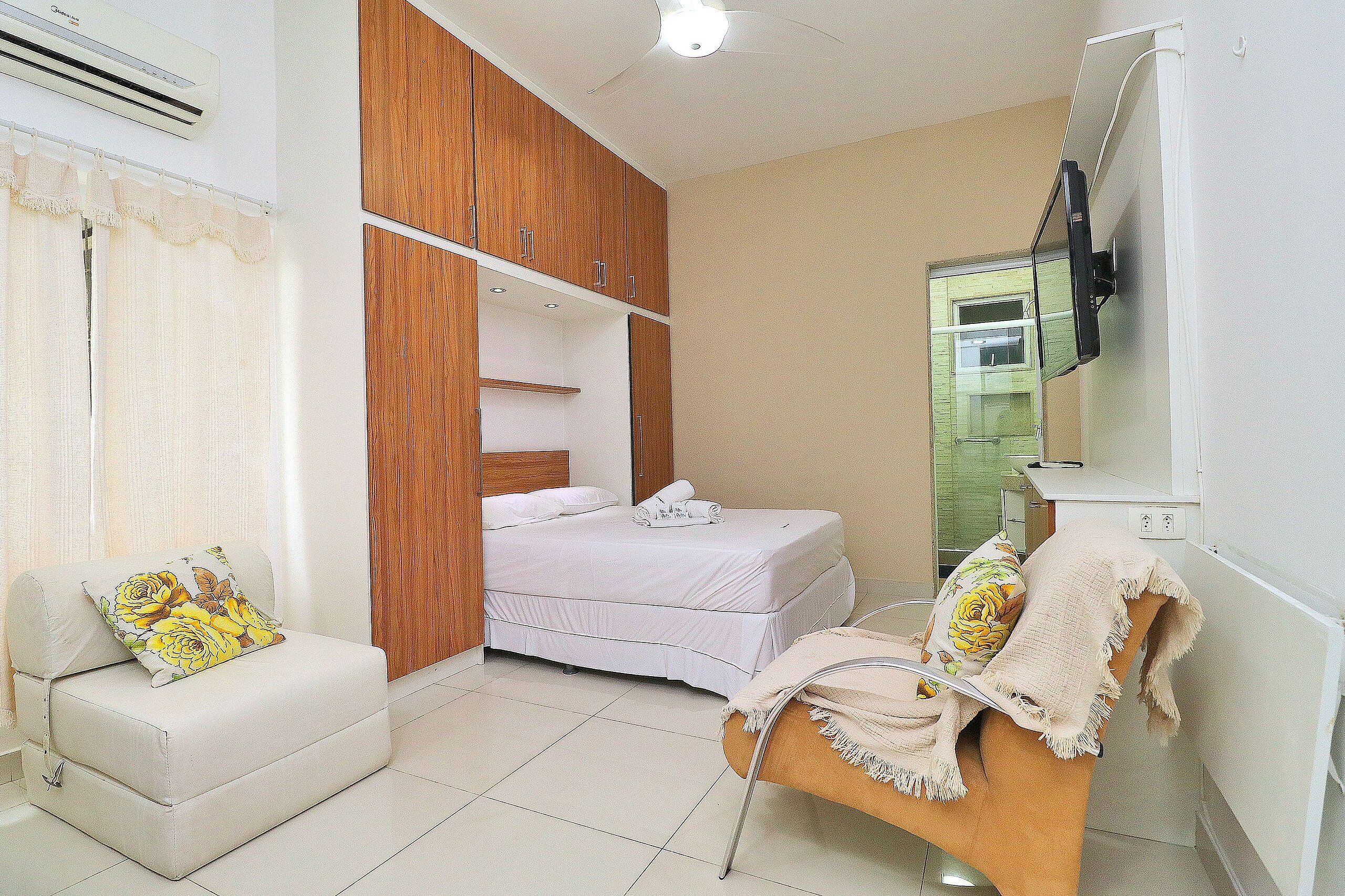 Une chambre à coucher comprenant un lit, un canapé, une armoire en bois et un téléviseur fixé au mur.