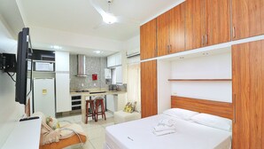 A bedroom with a bed, wooden wardrobe, and a kitchenette in the background. - Rio Spot Homes MC C055 (Rio de Janeiro)