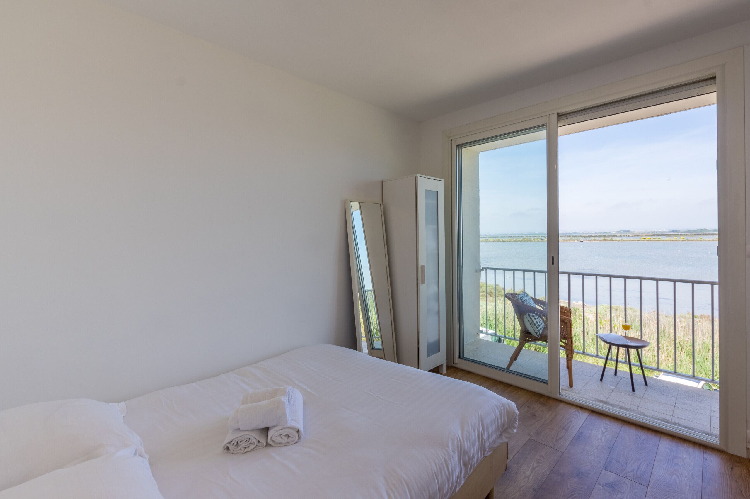 Une chambre d’hôtel avec un lit, un balcon doté d’une chaise et d’une table, et une vue sur la mer.